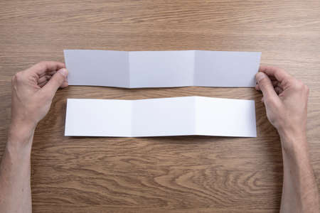 Mens hands holding empty white booklet on wooden background. View from aboveの写真素材