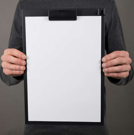 A man in a gray shirt holding plastic clipboard with a white booklet
