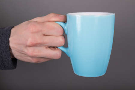 A man in a gray shirt holding a blue mugの写真素材