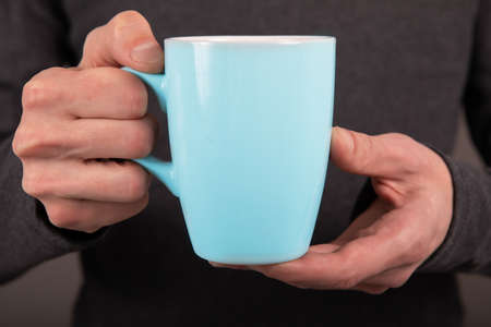 A man in a gray shirt holding a blue mug