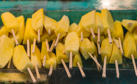 Many pieces of pineapple on wood sticks on the shelf at the marketの写真素材