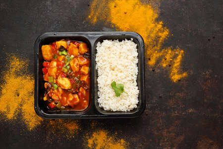 Dietary catering, Chinese chicken with white rice. Ready dish in a black container. Composed take-out meal, diet catering. The container on a dark background.の写真素材