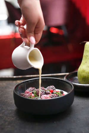 Fruit breakfast. Granola with fresh fruit. Granola with fresh fruit. The woman is pouring milk into the bowl. A bowl of milk and fresh fruit. A healthy nutritious breakfast.の写真素材