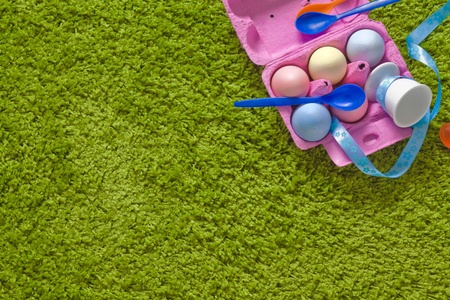 colored easter eggs and spoons in a egg-box on green background