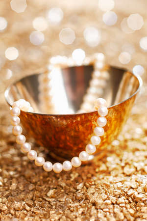 A matched string of pearls cascades down from a pretty silver bowl backed by a bokeh of festive party lightsの写真素材