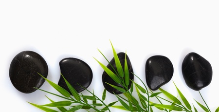 A row of spa massage stones and bamboo leaves on a white background with copyspaceの写真素材