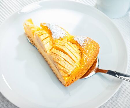 Slice of delicious golden freshly baked apple tart being served onto a white plate, high angle viewの写真素材