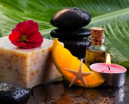 Soap block and orange slice resting on a table with basalt stones and oils for a spa break