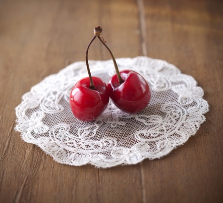 Closeup of two delicious ripe red sweet cherries joined by a common stalk on a lacy doilyの写真素材