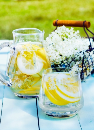 Lemon and cedar refreshment. Flowering Cedar Lemonade with water and citrus slices outdoors on a wooden table. A basket with blooming cedar in the backgroundの写真素材