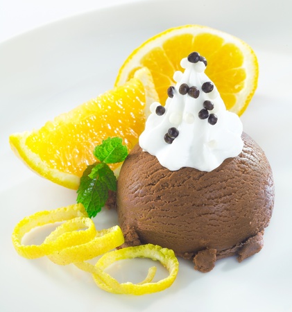 Gourmet chocolate icecream dessert topped with whipped cream and served with orange slices and zestの写真素材