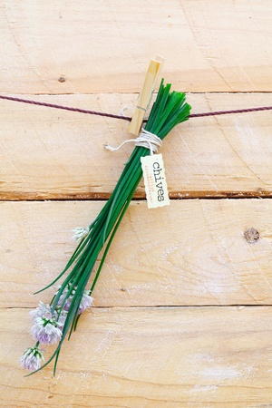 Bunch of fresh green chives with a decorative label hanging from a clothes peg against a rustic wooden backgroundの写真素材