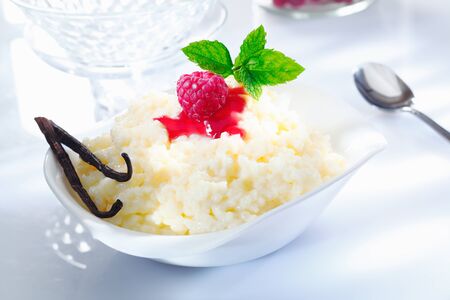 Fruity rice pudding dessert with raspberry topping and vanilla pods on white background.の写真素材