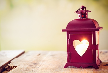 Decorative red metal lantern with a heart cutout lit by a glowing candle with copyspace for Valentines or Christmasの写真素材
