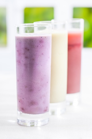 A tall glass of creamy blended yoghurt berry smoothie with a variety of other flavours in a receding row with shallow dofの写真素材