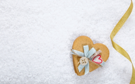 Snow background with a decorated heart shaped cookie and festive ribbon with copyspace for your Valentines or Christmas greetingの写真素材