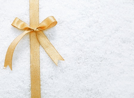 Decorative simple gold ribbon and bow on a background of winter snow with copyspace for your Christmas or festive greetingの写真素材