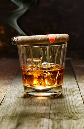 Burning Cuban cigar resting on a glass of brandy in a bar, the luxury pleasures of a wealthy macho manの写真素材