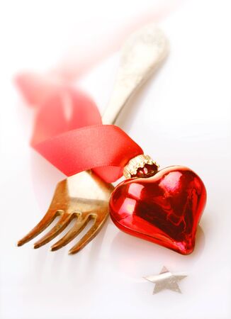 Romantic red heart decoration with twirled ribbon lying across a fork in a Christmas, Valentines, wedding or anniversary backgroundの写真素材