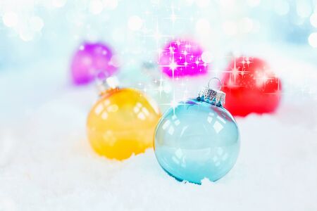 Delicate blue glass Christmas bauble on snow with additional twinkling colourful balls behind with shallow dof for a pretty wintery seasonal backgroundの写真素材