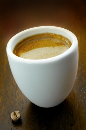 Closeup of a frothy cup of strong fresh espresso coffee with a single coffee bean on a dark wood backgroundの写真素材