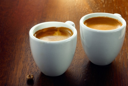 Two espresso coffees in small white cups,with a single coffee bean resting on the wood backgroundの写真素材