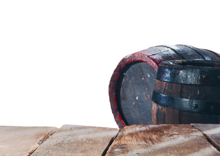 Old stained oak wine or beer barrels with metal bands behind an empty rustic timber table with planks for your food, beverage or product placement isolated on whiteの写真素材
