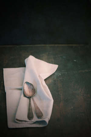 Folded plain white linen napkin and teaspoons on an old dark wooden table with copyspaceの写真素材