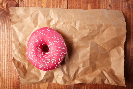 Overhead view of a pink strawberry doughnut with sprinkles on a sheet of crumpled grungy brown paper with copyspaceの写真素材