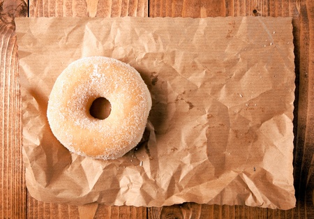 Overhead view of a round fresh sugar doughnut on crumpled brown paper with copyspace on a wooden backgroundの写真素材