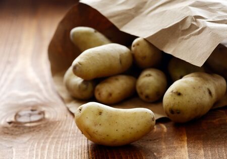 Farm fresh potatoes spilling out of a brown paper packet onto a rustic wooden table on the farmers marketの写真素材