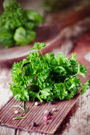 Bunch of fresh crinkly leafed parsley lying on a rustic wooden chopping board on a grunge wooden kitchen tableの写真素材