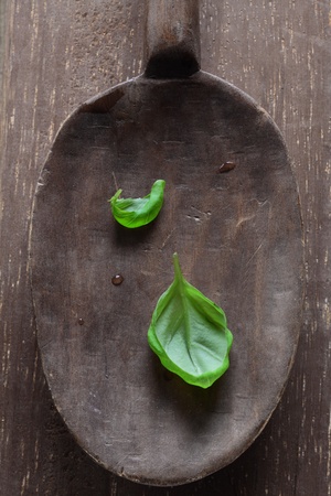 Overhead view of two fresh basil leaves in an old rustic vintage wooden ladleの写真素材