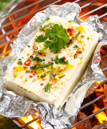 High angle view of a portion of feta or halloumi cheese topped with seasoning and spices grilling on a barbecueの写真素材
