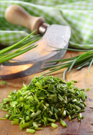 Pile of chopped fresh chives lying on a wooden kitchen table with a curved chopping knife and checked green and white clothの写真素材
