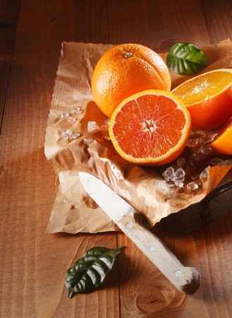 Two juicy oranges, one sliced in halves on brown paper and knifeの写真素材