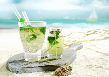 Refreshing cold Mojito cocktail with fresh mint served on an old wooden board lying on the golden sand of a tropical beachの写真素材