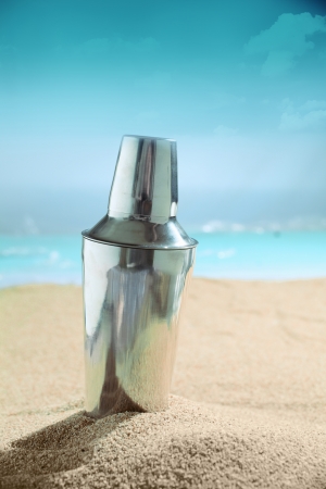 Modern metallic silver martini cocktail shaker standing on the golden sand of a tropical beach in the summer sunshineの写真素材