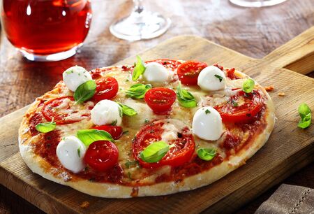 Delicious homemade freshly baked Italian pizza with a crisp golden crust garnished with fresh basil leaves served whole on an old wooden boardの写真素材