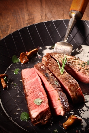 Rare cooked lean beef steak or fillet sliced through in a roasting pan during the cooking and preparation of a gourmet mealの写真素材