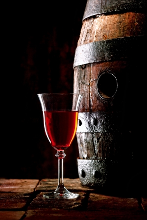A glass of red wine next to an old oak cask with its stopper out.の写真素材