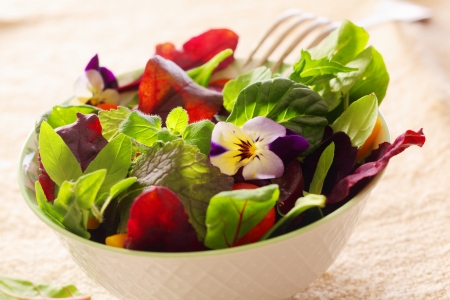 Fresh herb salad with leafy greens and nasturtium flowers served in a white ceramic bowlの写真素材