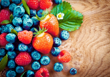 Overhead view of mixed ripe autumn berries including strawberries, raspberries and blueberries on a decorative woodgrain surfaceの写真素材