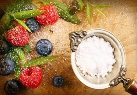 Fresh selection of mixed berries with granulated sugar in a strainer including raspberries and blueberries sprinkled with fine sugar on a wooden backgroundの写真素材