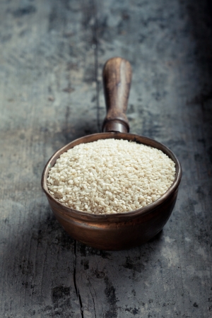 High-angle view of an old copper ladle filled with raw sesame over an old grungy grey wood tableの写真素材