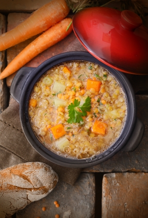 Top view of a warm and delicious freshly made pot of soup with raw carrots, chickpeas and a loaf of rustic breadの写真素材