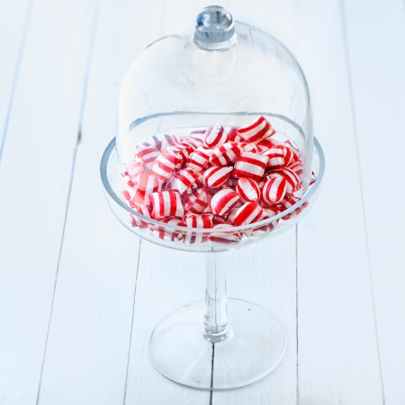 Colourful striped red and white candy in an elegant stemware glass container topped with a clear glass domeの写真素材