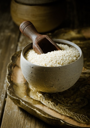 Couscous pasta , or steamed and crushed semolina wheat dough sold as dried granules for use as a cooking ingredient on an old tray with a wooden scoopの写真素材