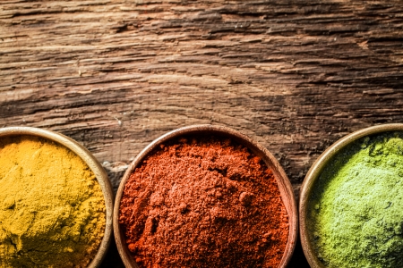 Close up overhead view of bowls of freshly ground curry, chilli and milled green tea, or matcha, spices on a textured wood background with copyspaceの写真素材