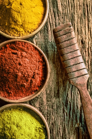 Closeup partial overhead view of bowls of ground green tea or matcha, chilli and curry spices with an old vintage wooden kitchen spatula on a textured wood backgroundの写真素材